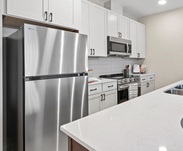 Modern kitchen with stainless steel fridge, stove, microwave, white cabinets, and a marble countertop island.