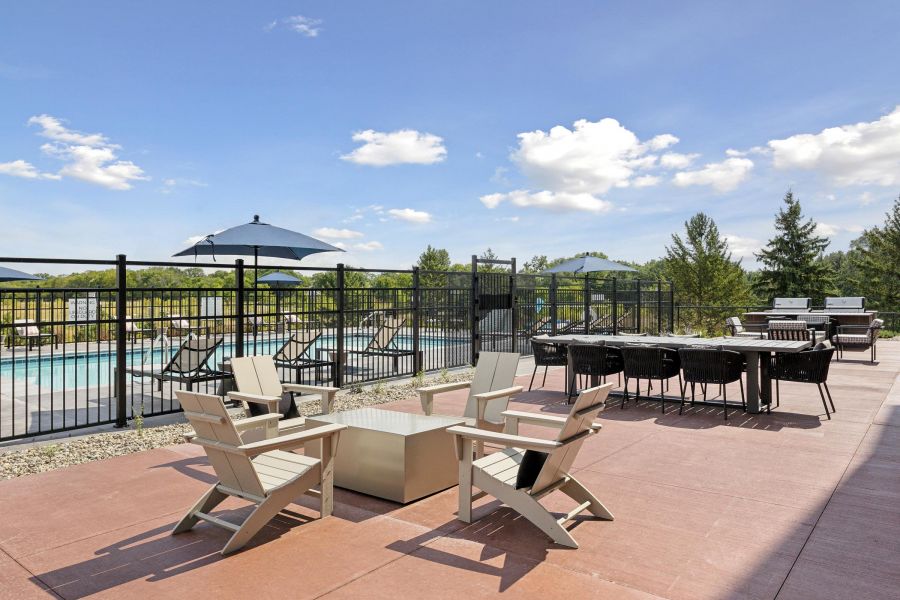 Outdoor patio with white chairs around a fire pit, dining table, grill, and pool in the background.
