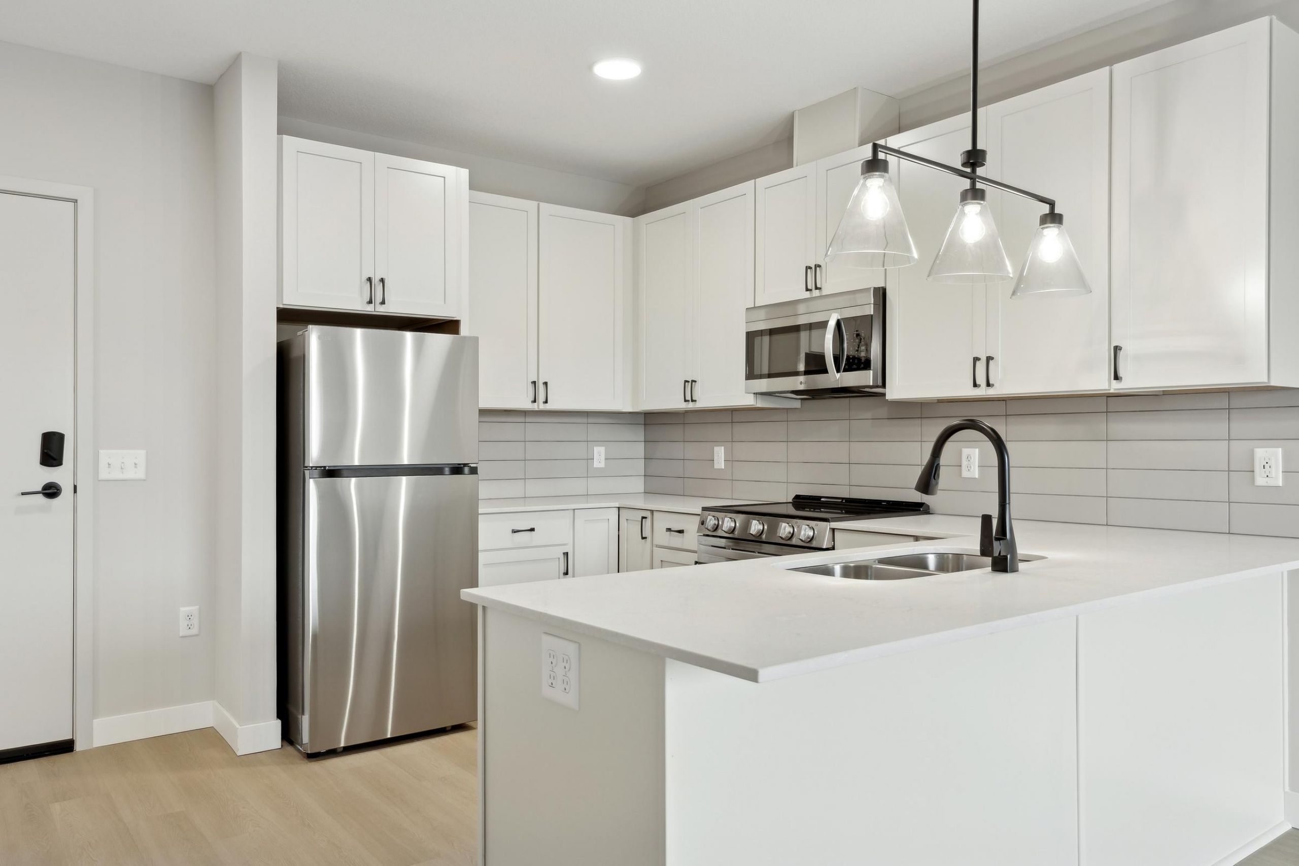 Modern kitchen with white cabinets, stainless steel appliances, and a white island with a black faucet.