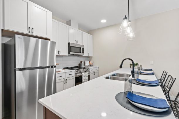 Modern kitchen with stainless steel appliances, white cabinets, and a breakfast bar set with blue napkins.