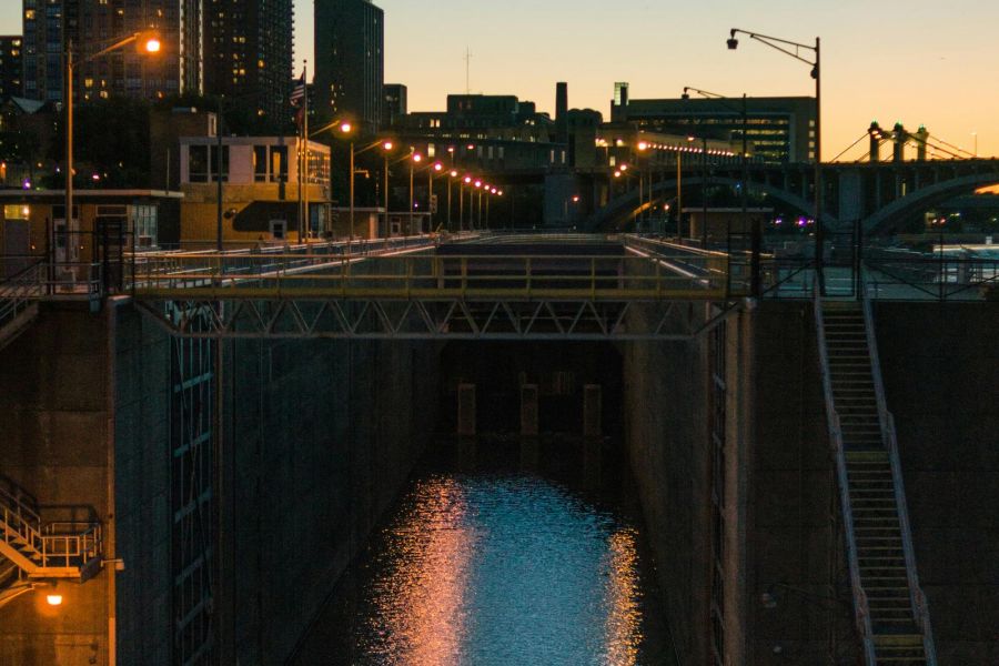 A lock with water reflecting city lights at dusk, with tall buildings in the background.