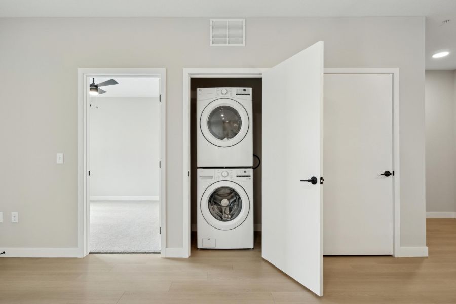 A stacked washer and dryer set inside an open closet in a modern, minimal laundry area.