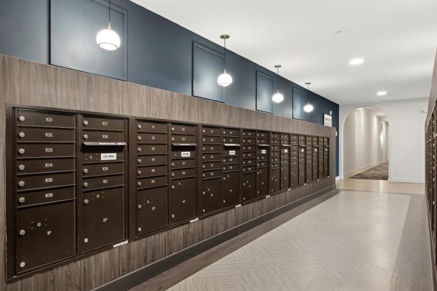 Mailboxes line a hallway wall in an apartment building, with pendant lights hanging from the ceiling.