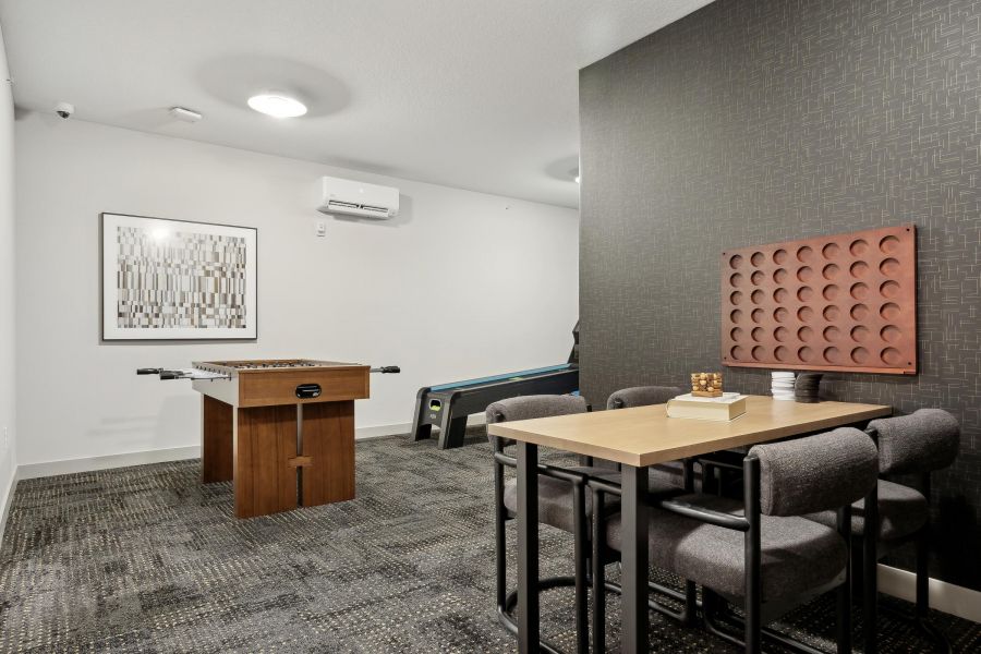 A game room with a foosball table, a Connect Four game, table, and chairs on a patterned carpet.
