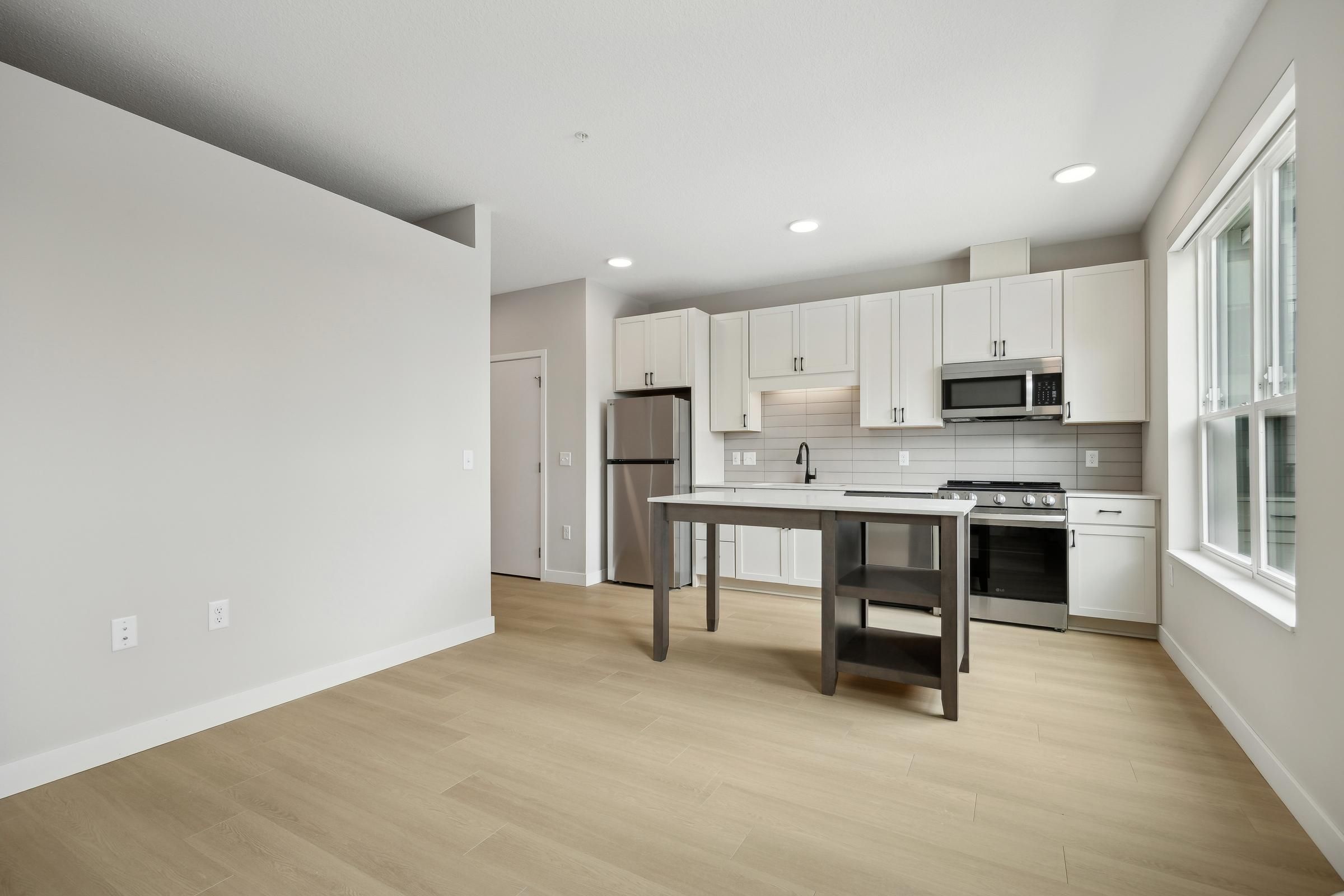 Modern kitchen with white cabinets, stainless steel appliances, island, and large window in a bright, empty space.
