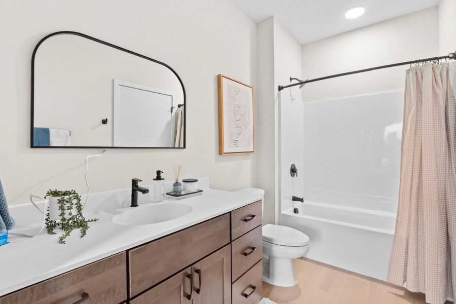Modern bathroom with a wooden vanity, large mirror, white sink, and a bathtub with a beige shower curtain.