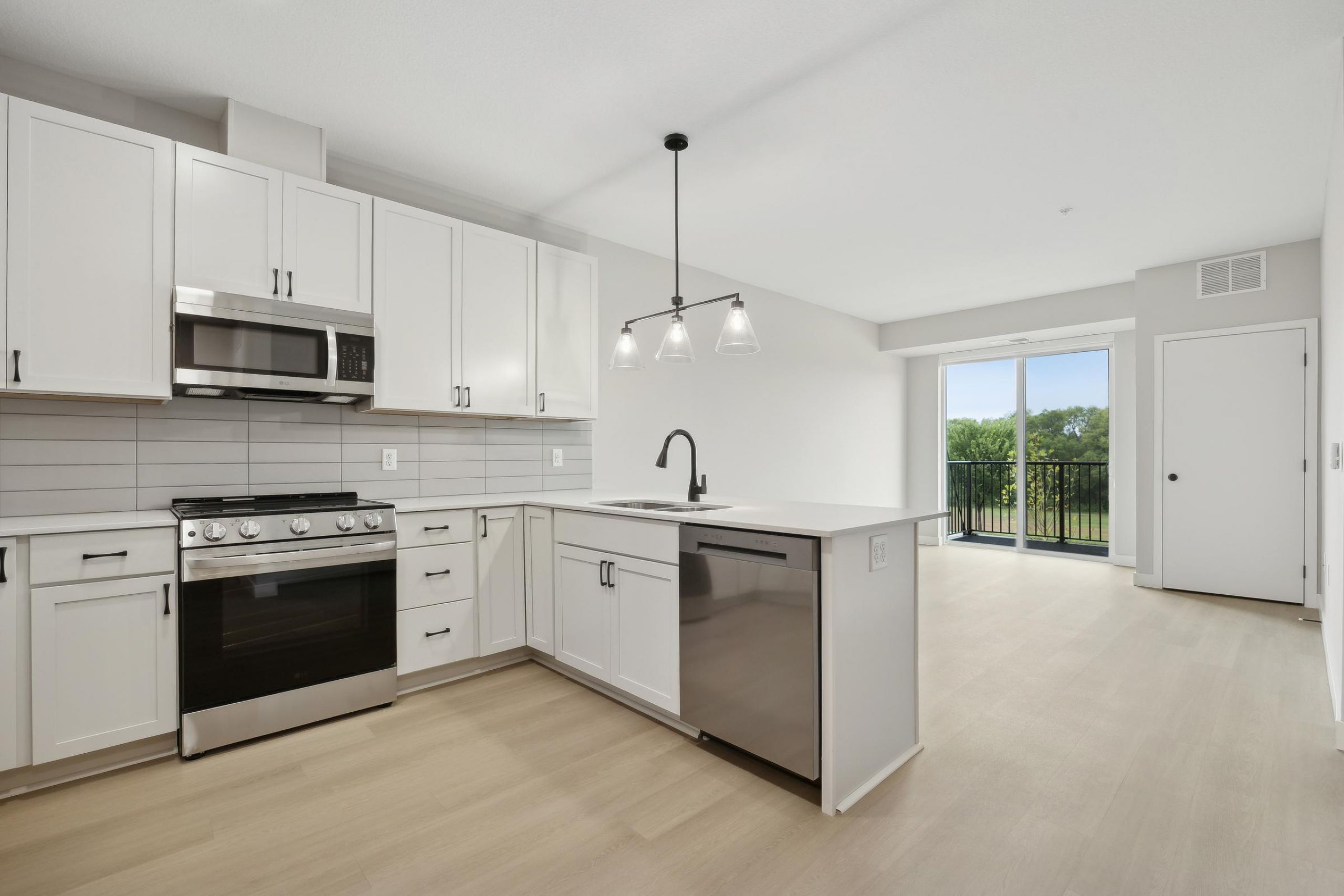 Modern kitchen with white cabinets, stainless steel appliances, and an island, opens to a bright living area.