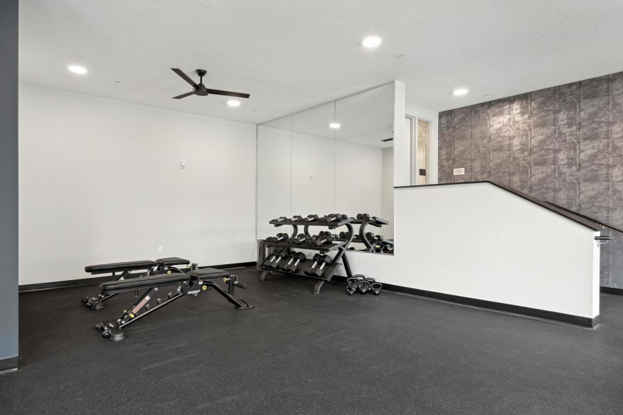 Modern home gym with two weight benches, a rack of dumbbells, mirrors, and neutral colored walls.