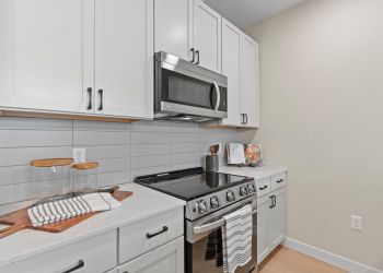 Modern kitchen with white cabinets, stainless steel appliances, and a striped towel on the oven handle.