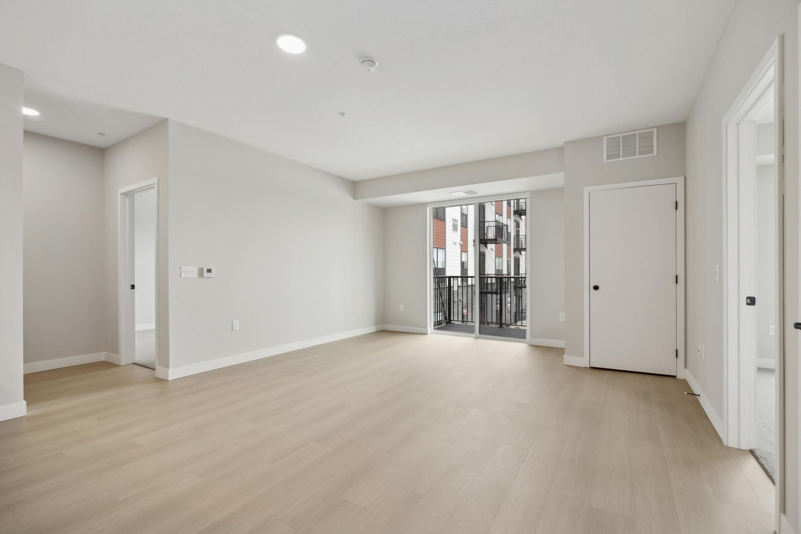 Bright, empty modern living room with light wood floors, white walls, and a balcony door.