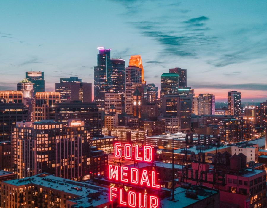 A neon "Gold Medal Flour" sign glows with a city skyline at dusk in the background.