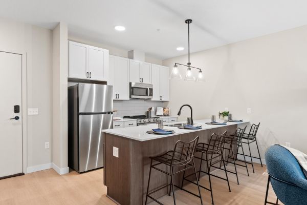Modern kitchen with white cabinets, stainless steel appliances, and an island with bar stools and place settings.