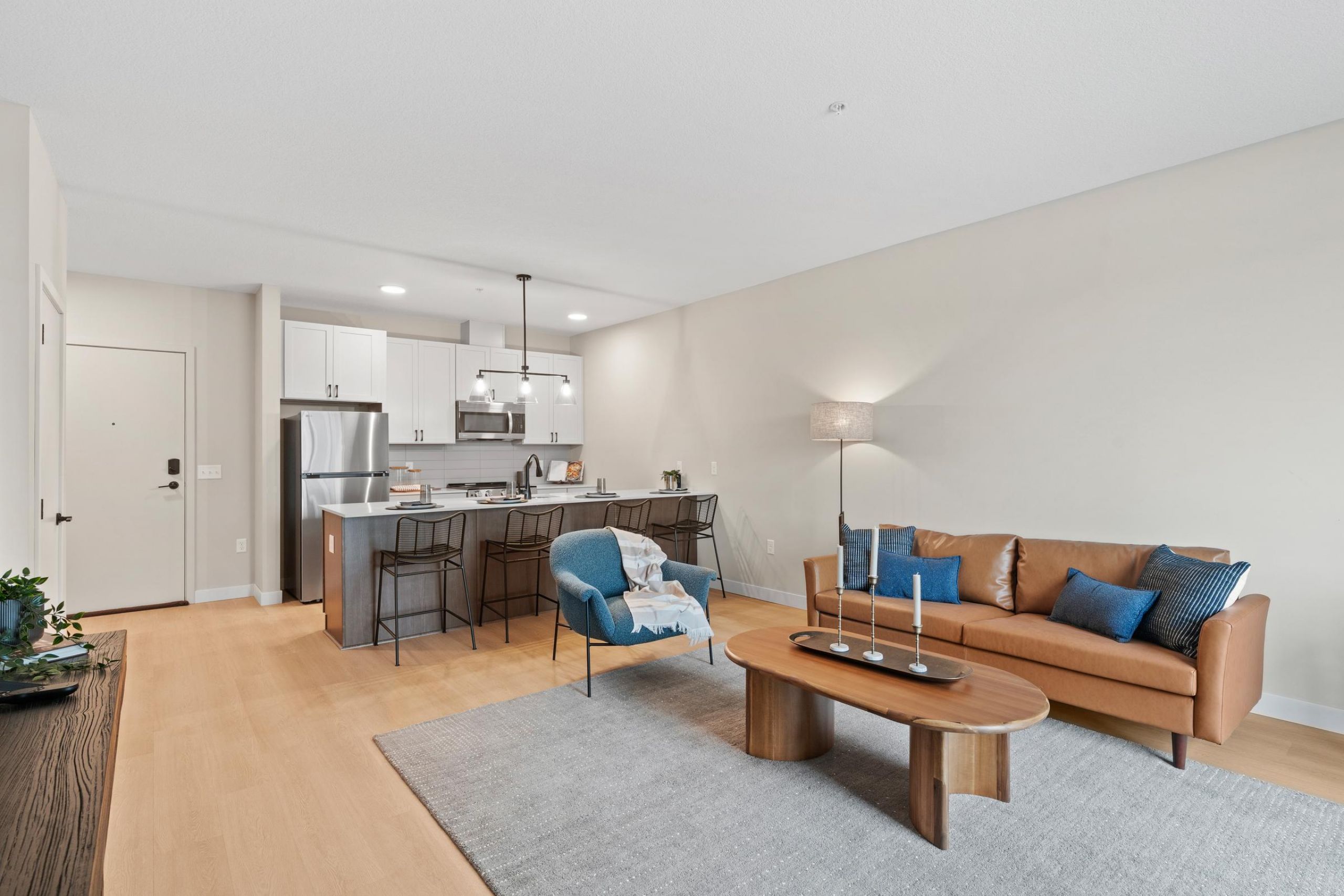 Modern open-concept living room and kitchen with neutral tones, stylish furniture, and stainless steel appliances.