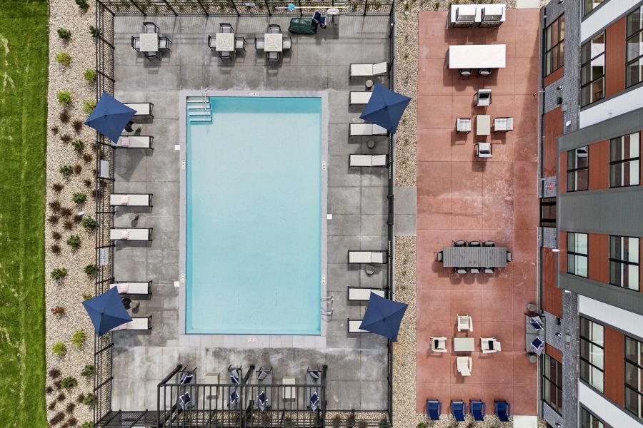 Aerial view of a rectangular outdoor pool with lounge chairs, umbrellas, and patio seating areas nearby.