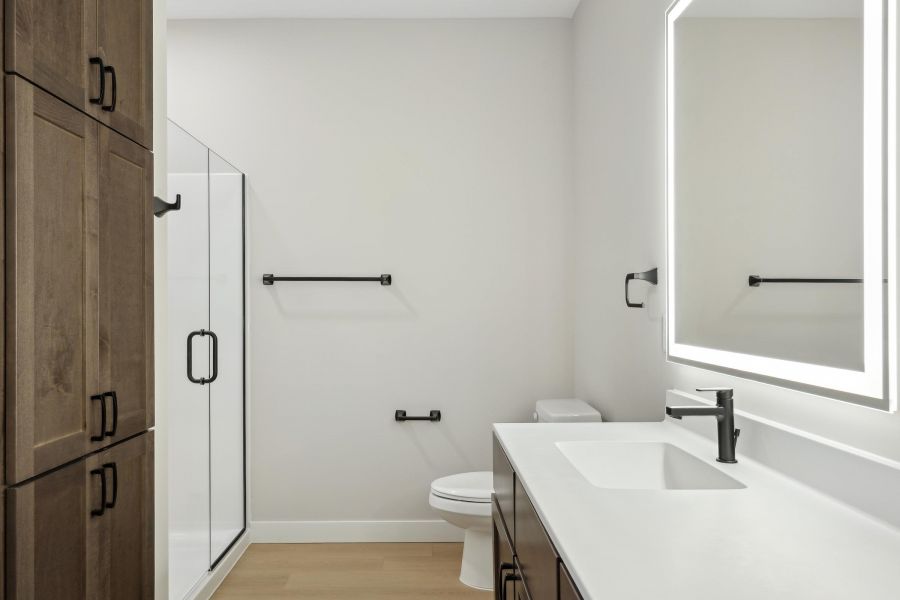 Modern bathroom with a glass shower, wood cabinets, lighted mirror, and black fixtures.