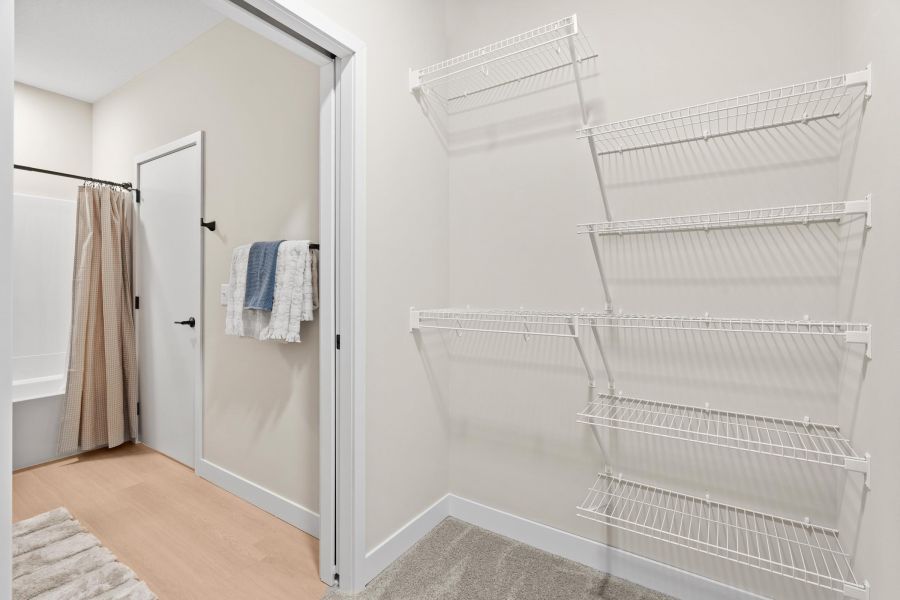 Empty wire shelves and a doorway leading to a bathroom with towels hanging on a rack and a shower curtain.