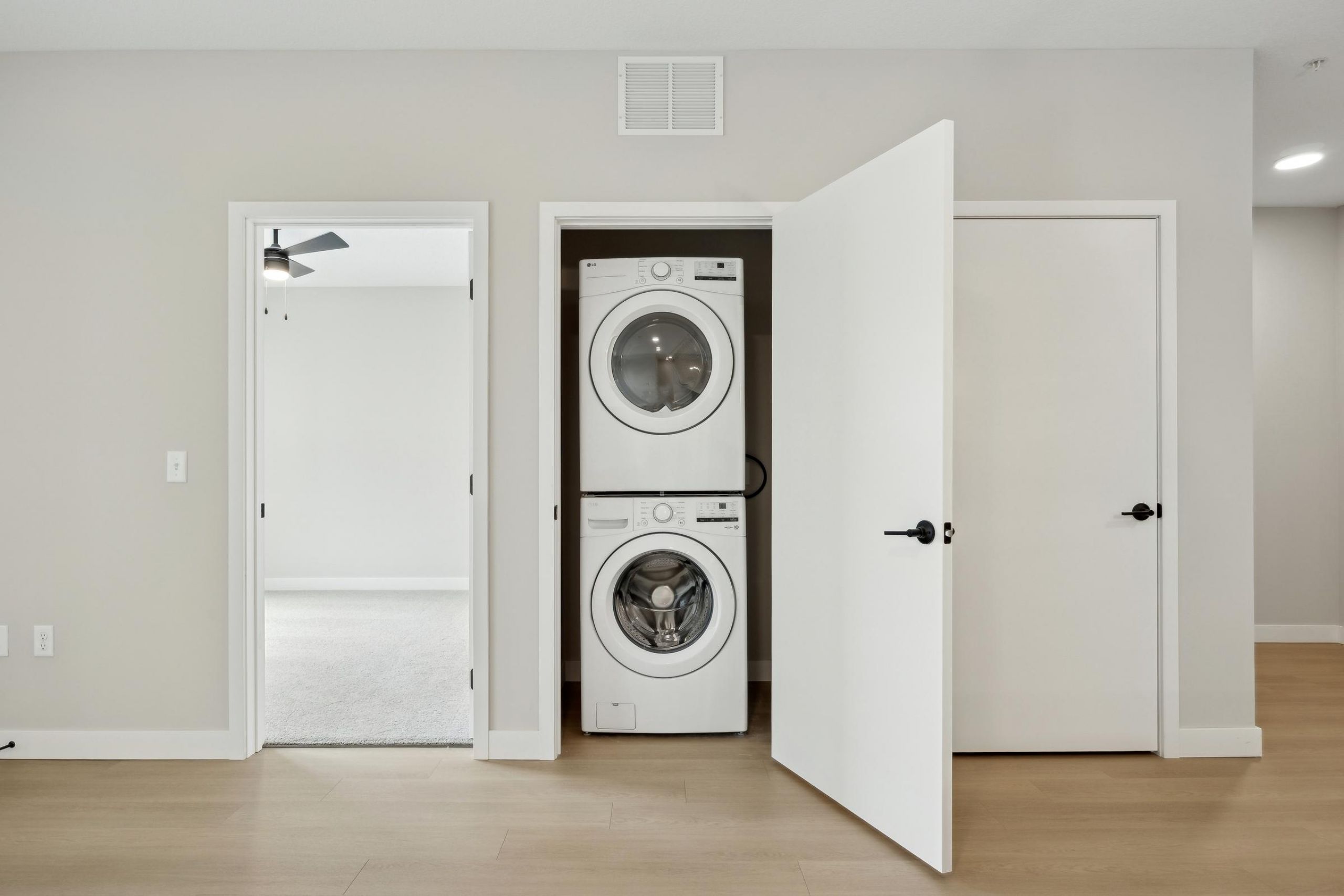 A stacked washer and dryer set inside an open closet in a modern, minimal laundry area.