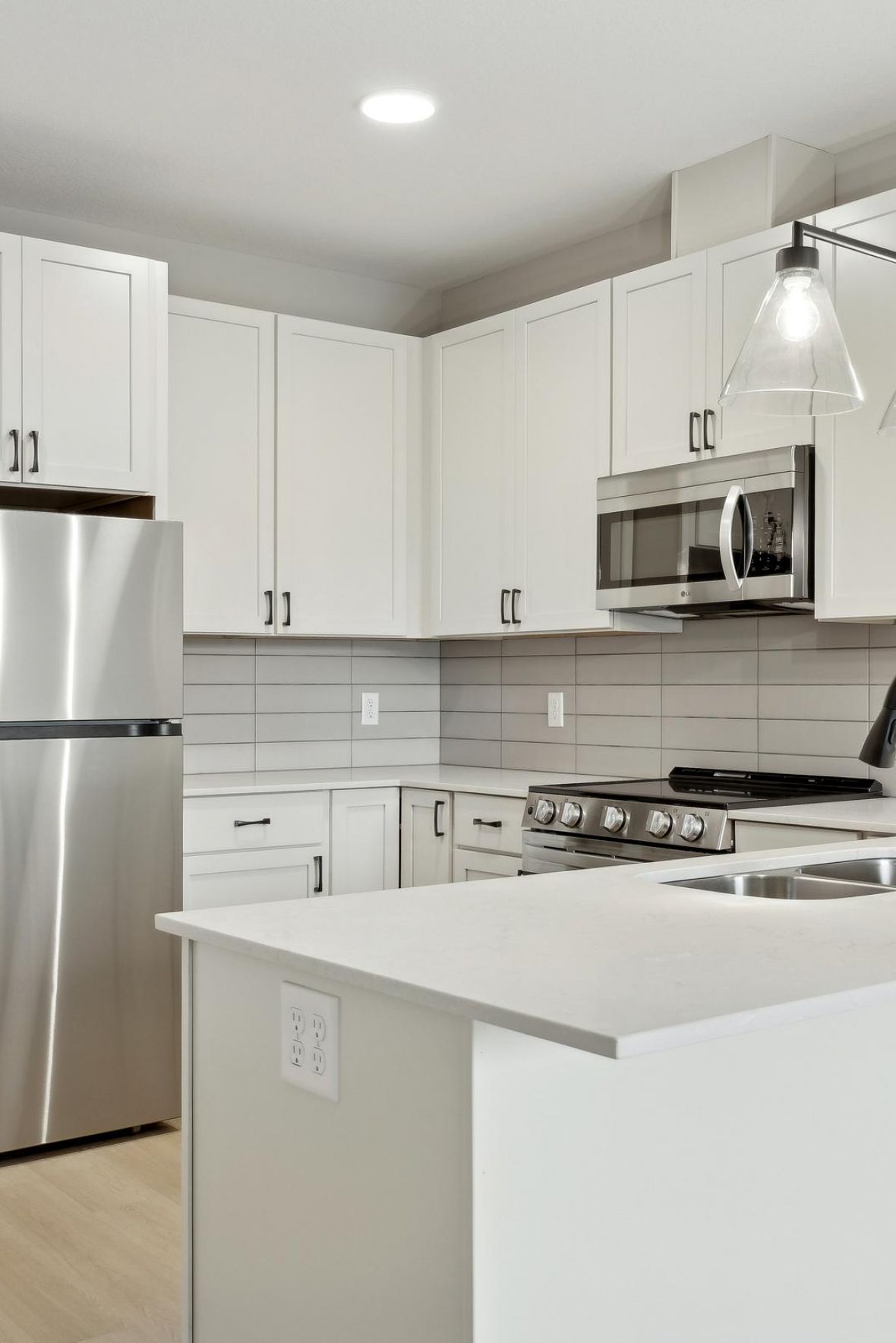 Modern kitchen with white cabinets, stainless steel appliances, and a white island with a black faucet.
