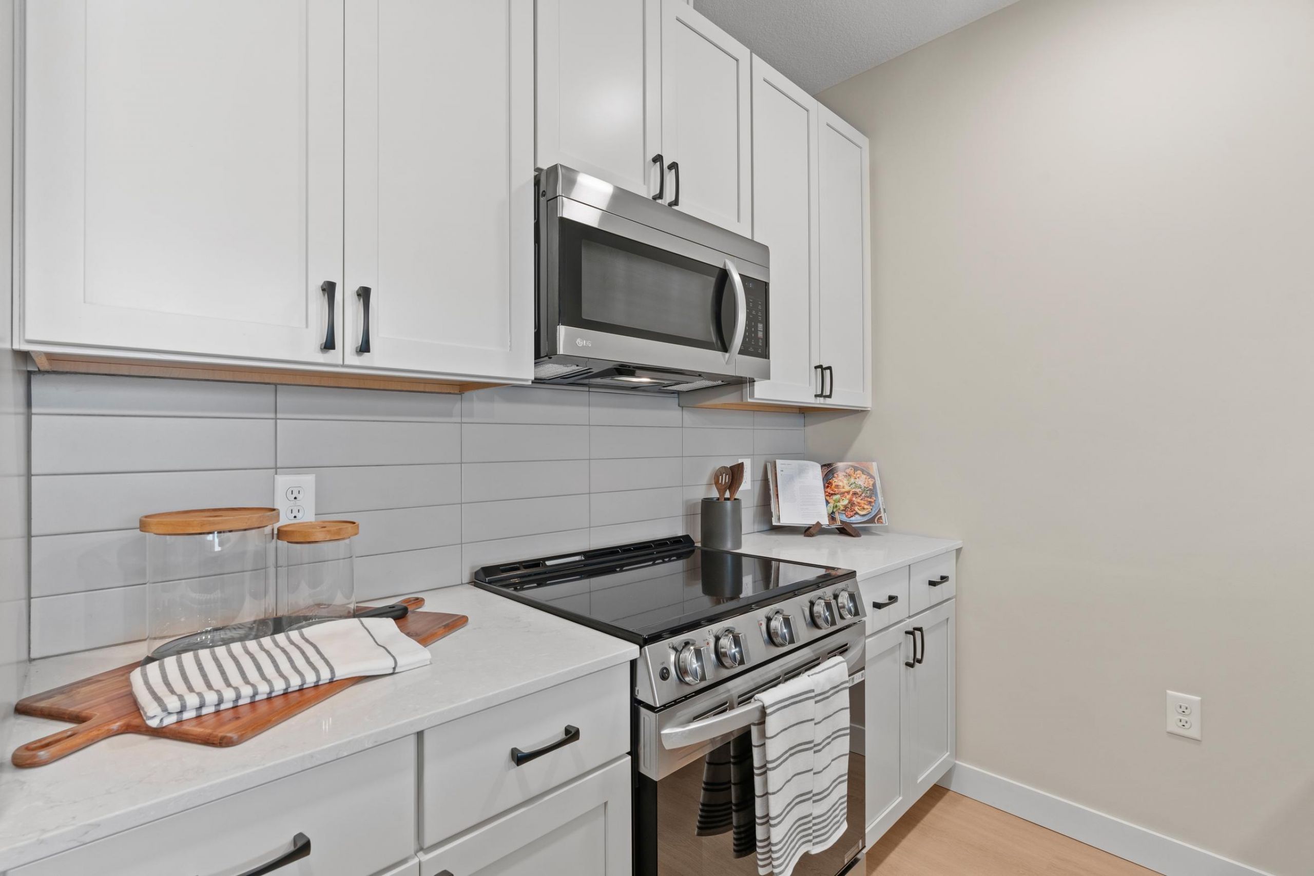Modern kitchen with white cabinets, stainless steel appliances, and a striped towel on the oven handle.