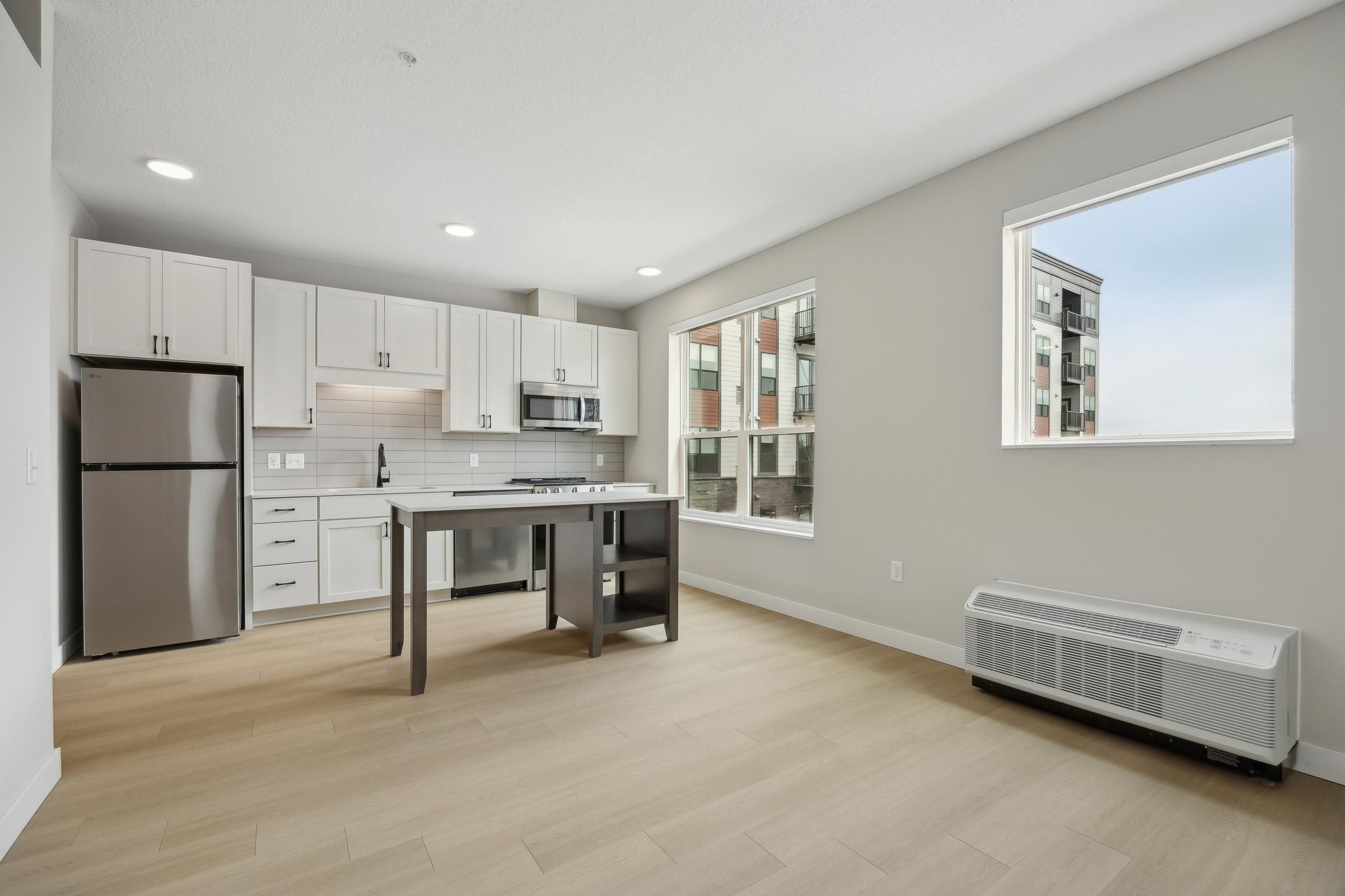 Modern kitchen with white cabinets, stainless steel appliances, island, and large windows with city views.