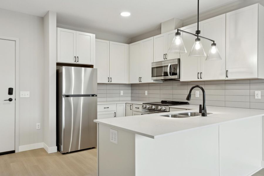 Modern kitchen with white cabinets, stainless steel appliances, and a white island with a black faucet.