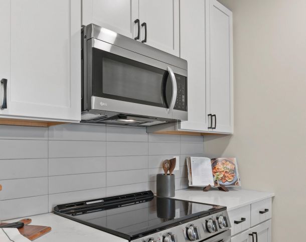 Modern kitchen with a stainless steel microwave above a stove, white cabinets, and an open cookbook on the counter.