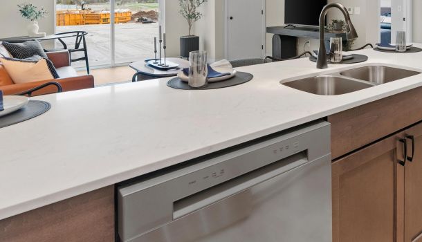 Modern kitchen island with a sink, dishwasher, and place settings, overlooking a bright living area.