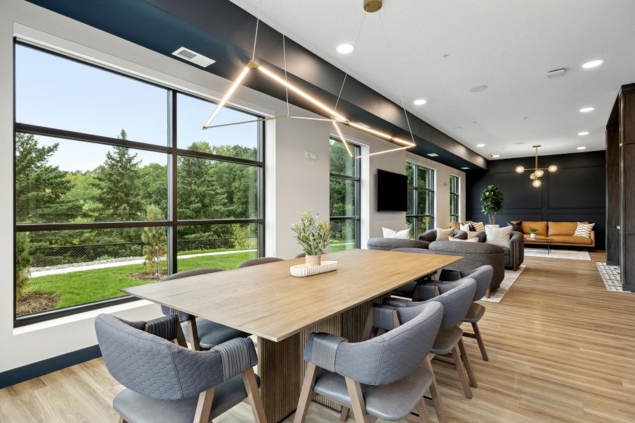 Modern dining and living area with large windows, gray chairs, and a view of green trees outside.