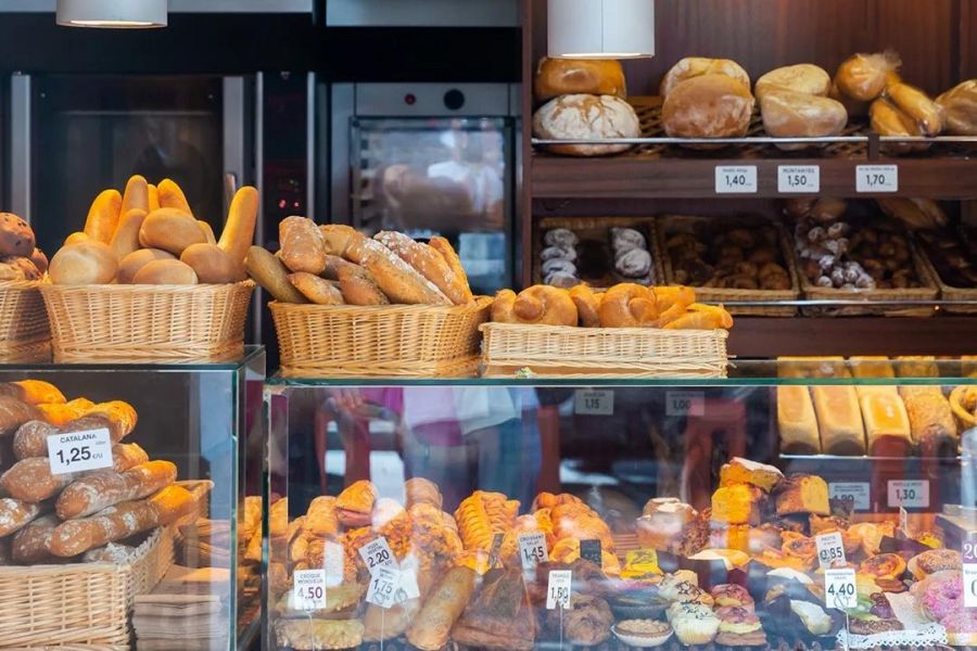 Bakery display with baskets and shelves full of assorted breads, pastries, and price tags.